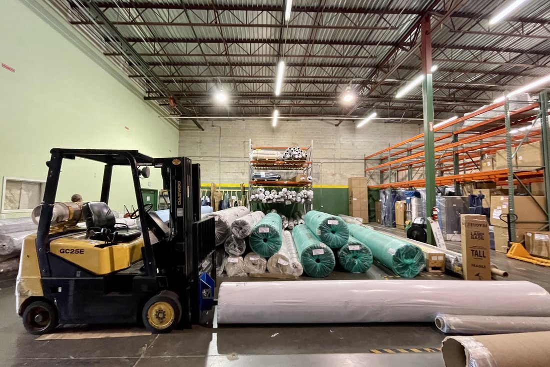 Wrapped rolled rugs staged beside a forklift inside the Bonita Springs storage warehouse.